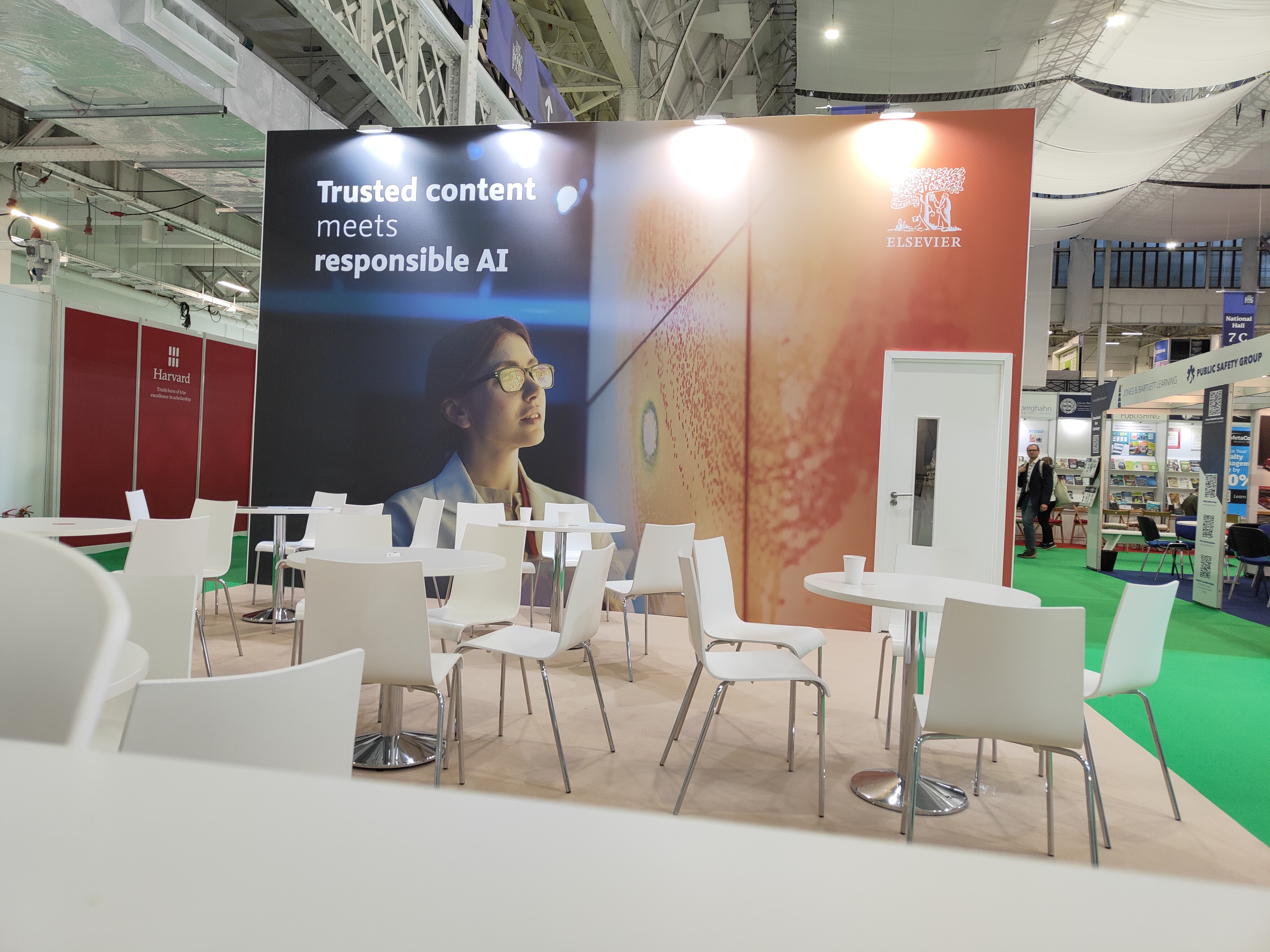 A booth at the close of the London Book Fair featuring a prominent banner for Elsevier with the text 'Trusted content meets responsible AI' and a thoughtful individual in a lab coat, alongside empty white tables and chairs.
